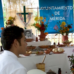 A young man in traditional Yucatecan costume sits in front of the Ayuntamiento's official Hanal Pixán altar. <a href=></a>