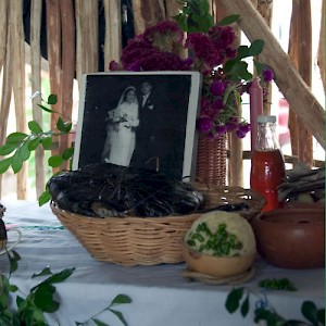 Mucbil Pollo wrapped in banana leaves sits in a basket in front of a photo of a married couple, long since passed away. <a href=></a>