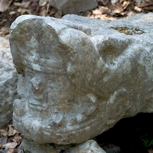 The face of a warrior in the mouth of the winged serpent, Kukulkan, discarded near a jungle path. <a href=></a>